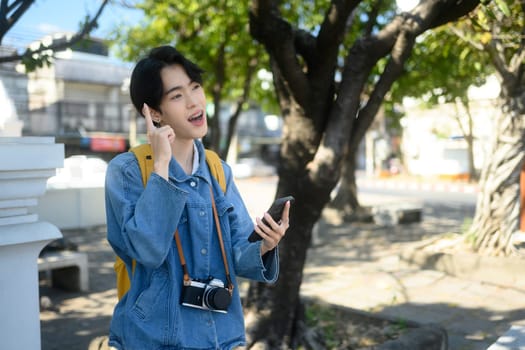 Young traveler with camera around their neck using mobile phone in a sunny urban. Exploration and travel concept.