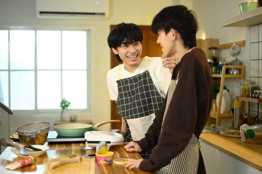 Happy gay couple in aprons preparing a delicious meal together in modern kitchen..