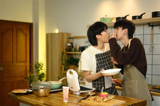 Loving male gay couple preparing a delicious breakfast at counter in warm kitchen.
