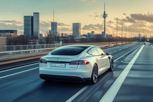 A white electric vehicle glides smoothly on an urban highway during sunset, surrounded by tall buildings and a clear sky.