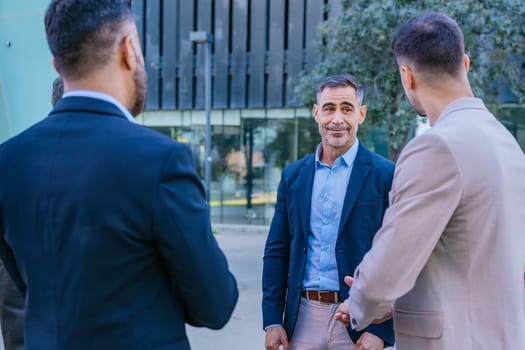 A group of business professionals engaged in a serious discussion outdoors. They are dressed in formal and smart casual attire, with a modern cityscape in the background.