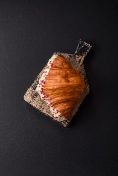 Crispy sweet red croissant with pistachio, raspberry and strawberry on a dark concrete background