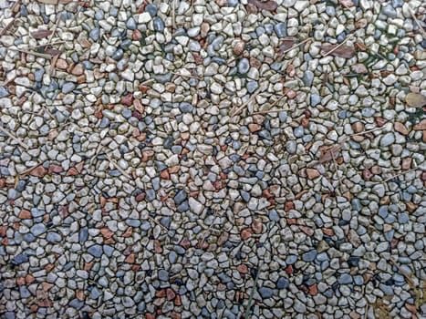 A variety of small pebbles in different colors covers the ground in a garden. These stones create an interesting and colorful texture under the warm sunlight. Natural elements surround the pebbles.