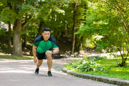 Athletic young man starting a running race in sunny park. Active Japanese sportsman jogging in summer forest during a morning workout. Confident Asian runner athlete, sport healthy lifestyle concept.