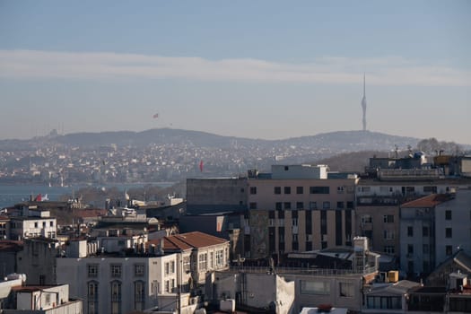 Elevated view of Istanbul's cityscape. Densely packed buildings, hills, and a distant communication tower under a clear sky. Water body visible in the background.