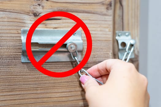 Hand unlocking a door chain lock with a red prohibition sign symbolizing security or restricted access concept