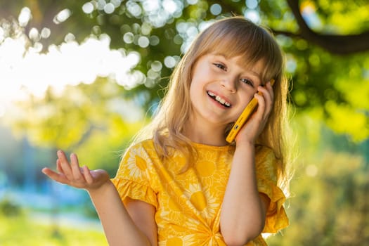 Happy preteen child kid having remote conversation communicate speaking by smartphone. Lovely blonde girl daughter talking with mother on phone good news gossip standing on city sunset park street