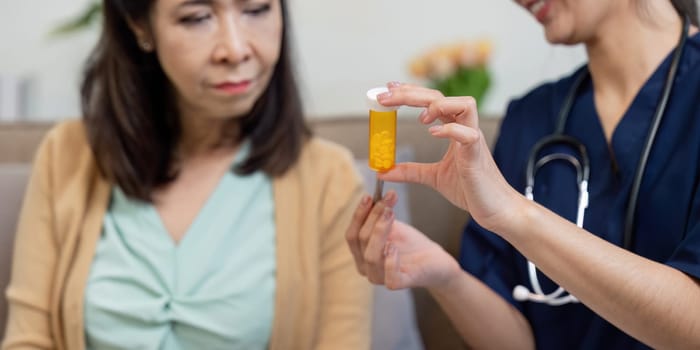 A caregiver holds up a medication bottle while explaining its use to an elderly woman, highlighting the importance of patient education in medication management.