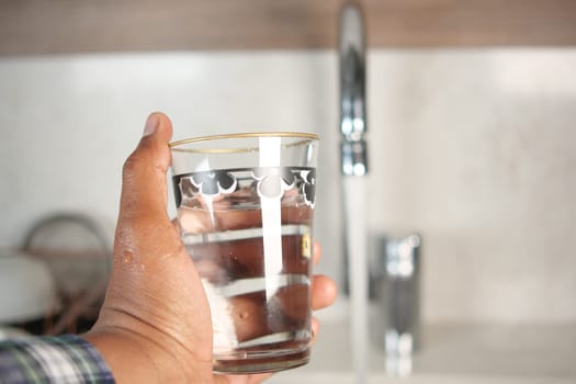 Close-Up of a Hand Holding Glass of Water by a Faucet.