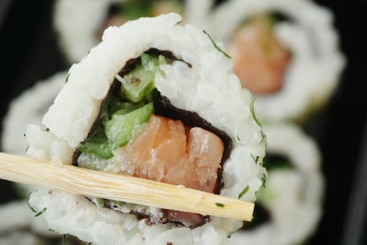 Colorful sushi roll presented with chopsticks, showcasing fresh seafood and greens.