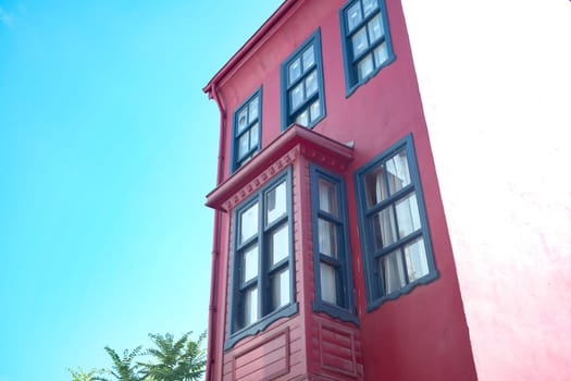 A visually striking and vibrant red house adorned with multiple windows against a bright blue sky