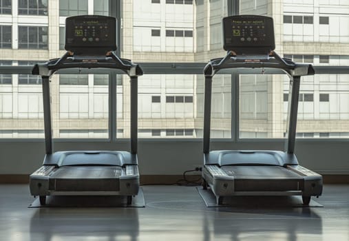 Bangkok, Thailand - Jan 18, 2025 - Back view of Two treadmill machines in fitness center. Looking outside through the Glass wall panels can see view building. use it as your Wallpaper, Poster and Space for text, Selective focus.