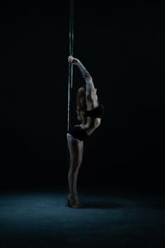 Graceful tattooed woman wearing lingerie dancing on pylon profile view in the dark room