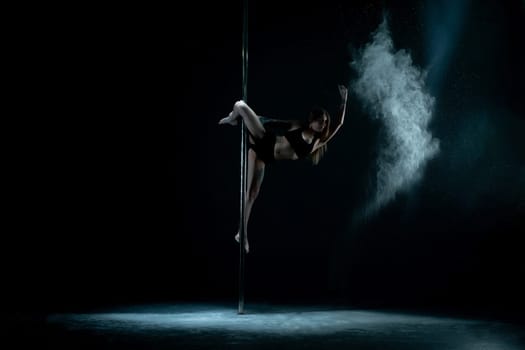 Beautiful girl wearing lingerie and high heels dancing on pylon in dust cloud view in the dark room