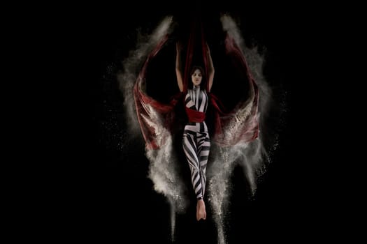 Beautiful woman wearing striped body dancing on cloth in white dust cloud shot in the dark