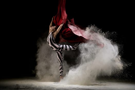 Beautiful girl wearing striped body dancing on cloth in white dust cloud profile shot in the dark