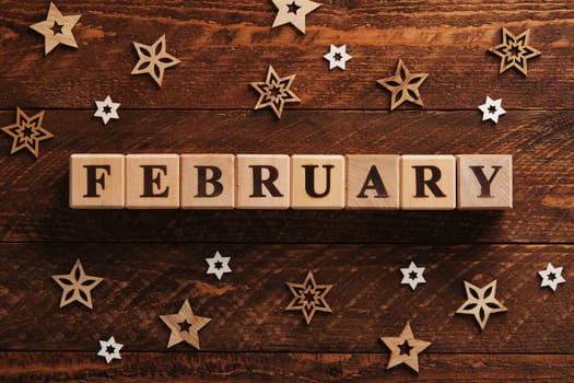Word February written in English with wooden blocks. Brown wooden background with stars