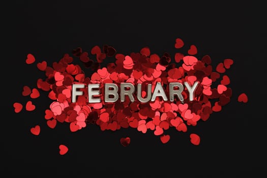 Text of white metallic letters February in English on the background with red heart confetti