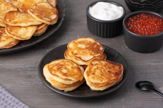 Delicious stack of golden pancakes served with cream and caviar on a rustic table.