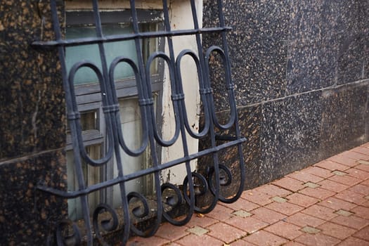 Black metal wrought iron grating on the basement windows. The building is a sidewalk. Security. The facade of the building.