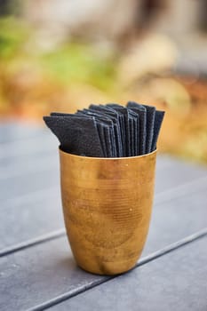 Black paper napkins in a copper cup. Serving. An outdoor cafe. Indian cuisine.
