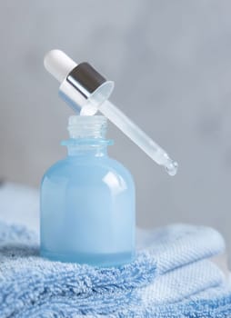 Drop falling from pipette set on opened blue glass dropper bottle on blue towel against grey close up, mockup. Natural serum or essence