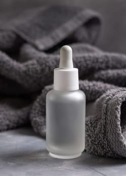 Clear glass dropper bottle with pipette near dark grey towel closeup, brand packaging mockup, copy space. Natural handmade cosmetic product for facecare and spa procedures - serum or essence