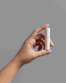 Female hand white opened lip balm stick against grey close up, cosmetic package mockup, copy space. Lip care beauty product with minimal composition