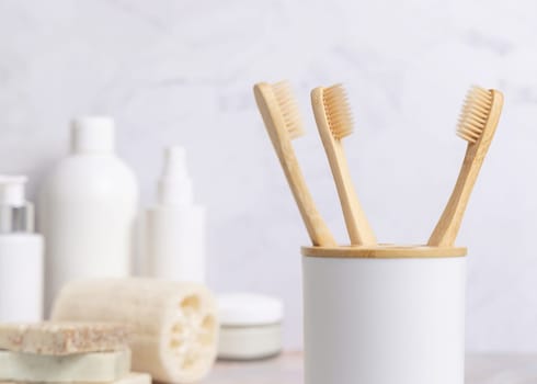 Eco-friendly wooden bamboo toothbrushes in holder cup in a white in bathroom against natural cosmetics, mockup. Zero waste concept, personal care and hygiene products