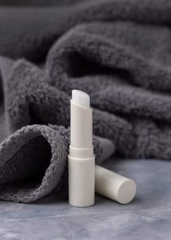 Opened white blank lip balm stick on dark grey folded towels closeup, cosmetic packaging mockup, copy space. Lipcare beauty product for mens everyday personal care