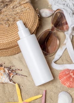 White blank spray bottle, sunglasses, towel, starfishes and shells on a sandy beach, top view. Sunscreen cosmetics mockup. Summer vacation and spf uv-protecting skin care concept