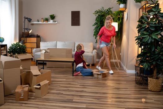 In a cozy living room with greenery, a mother and child happily unpack boxes, enjoying each others company