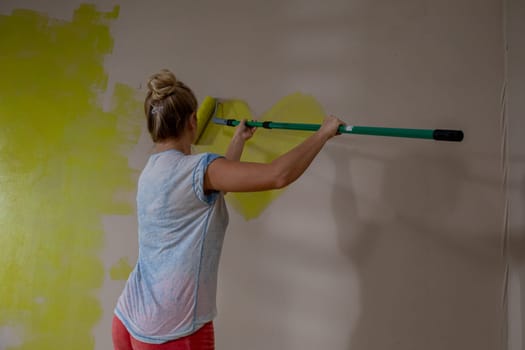 A person enthusiastically applying bright yellow paint to a wall using a paint roller for a home makeover project