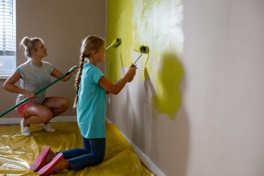 A devoted mother supervises her daughter as they joyfully paint a room vibrant green in a fun DIY project