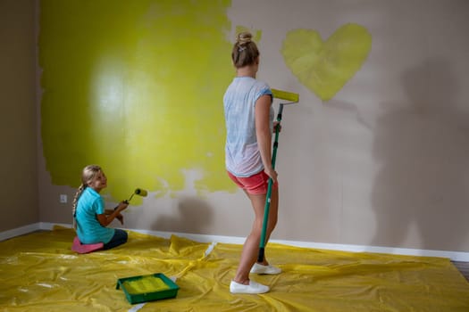 Two smiling individuals paint a wall with a heart design using vibrant, bright colors in a delightful scene