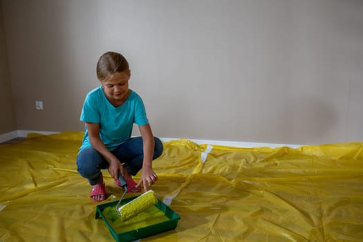 A child excitedly gets ready to paint a whole room using a roller while standing on a bright yellow plastic sheet
