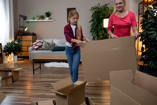 A delighted child and a caring adult cheerfully unpack a variety of cardboard boxes in a cozy living room setting