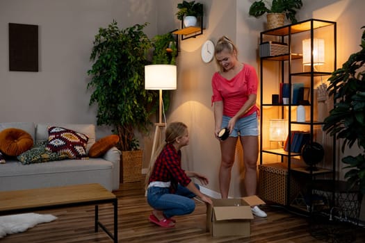 Women are joyfully unpacking a large box filled with items in a stylish and cozy living room setting