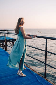 A woman in a flowing green dress poses on a pier by the sea at sunset, with a Turkey flag waving in the background.