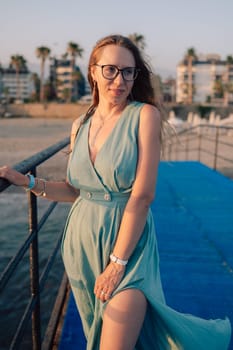 A woman in a flowing green dress poses on a pier by the sea at sunset, with a Turkey flag waving in the background.