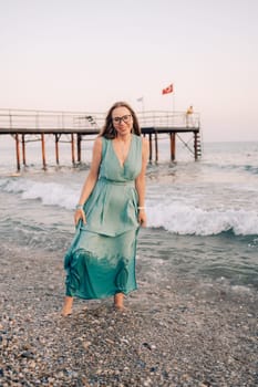A woman in a flowing green dress poses on a pier by the sea at sunset, with a Turkey flag waving in the background.