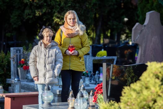 A mother and her young child visit a peaceful cemetery, honoring family with candles and vibrant flowers