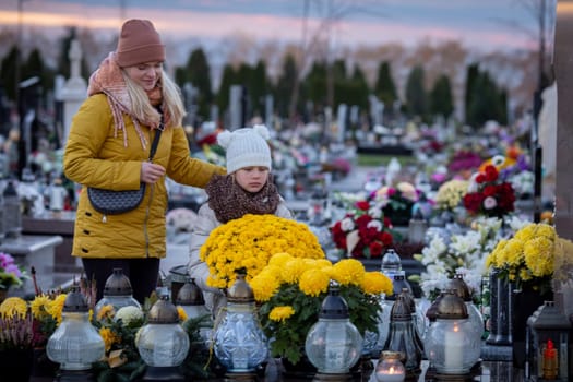 In a tranquil cemetery, a touching moment of remembrance unfolds, showcasing a mother and child amidst floral tributes