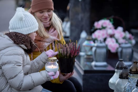 Two women gather at a peaceful cemetery, honoring loved ones with lanterns and fresh flowers placed gently