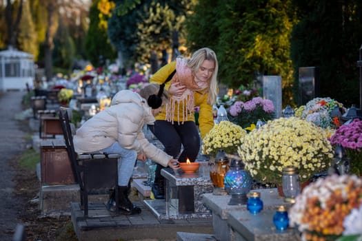 Two people visit a cemetery to honor a loved one, lighting candles and placing fresh flowers at the gravesite