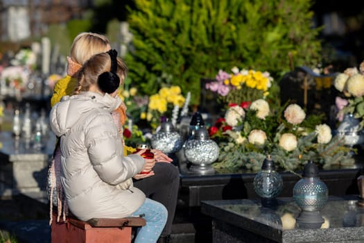 Two individuals reflect on their loved ones among vibrant flowers in a serene cemetery, filled with memories