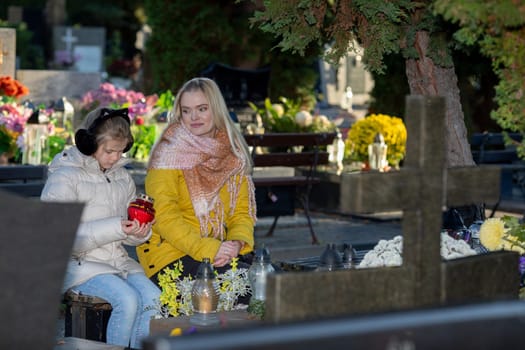 Two women sit quietly in a serene cemetery with vibrant flowers, sharing a deep, thoughtful moment together