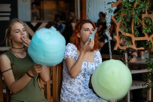 Two girls savoring colorful cotton candy in a lively caf setting