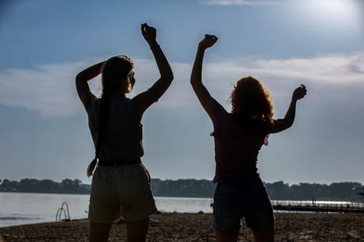 Two joyful figures gracefully dance together by the water, framed by a breathtaking sunset backdrop that enchants