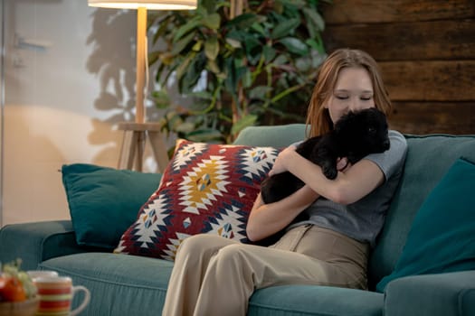 A young girl enjoys a cozy, delightful moment on the couch with her adorable black cat in a warm, inviting living room